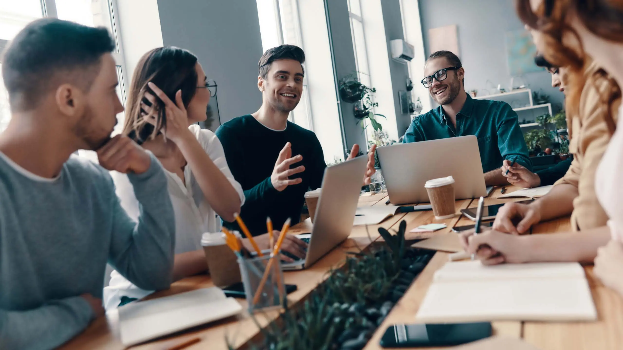 Achieving success together. Group of young modern people in smart casual wear discussing something and smiling while working in the creative office