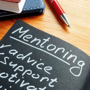 White text on a black chalkboard-looking piece of paper. The title is "Mentoring" and there is a checklist of advice, support, motivation.